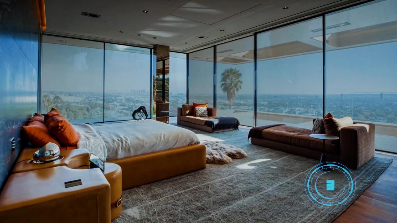 Quarto amplo com paredes de vidro do chão ao teto no modo transparente, vista livre para a cidade e horizonte ao entardecer, cama com almofadas em tom terracota, sofás de couro marrom, tapete cinza, decoração moderna e sofisticada, iluminação natural suave, fotografia realista